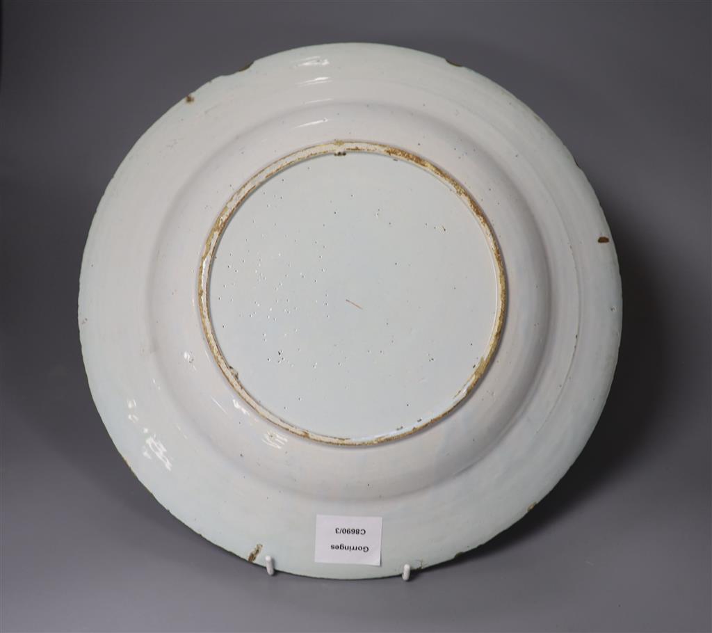 A large polychrome Delft charger, painted with a central figure beside a walled garden, set within floral borders, in the Chinese taste